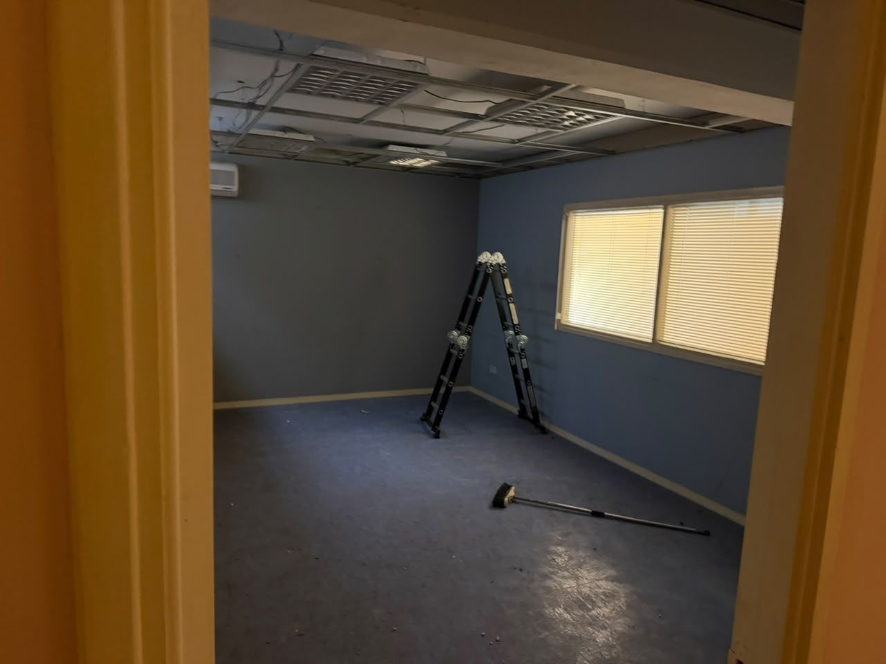 An empty training room with blue walls, a ladder and a window, before renovation